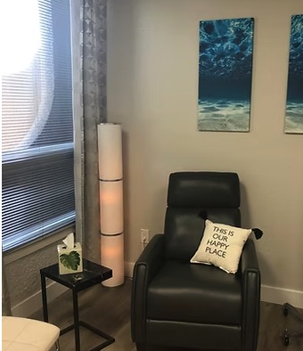 A calm treatment room with a comfortable recliner, ocean-themed art, and natural light